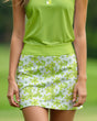 A woman wearing a green golf polo and a floral golf skirt.