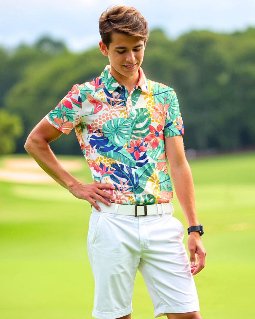 A young man stands on a golf course, wearing a colorful floral golf polo, white shorts, and a white belt.