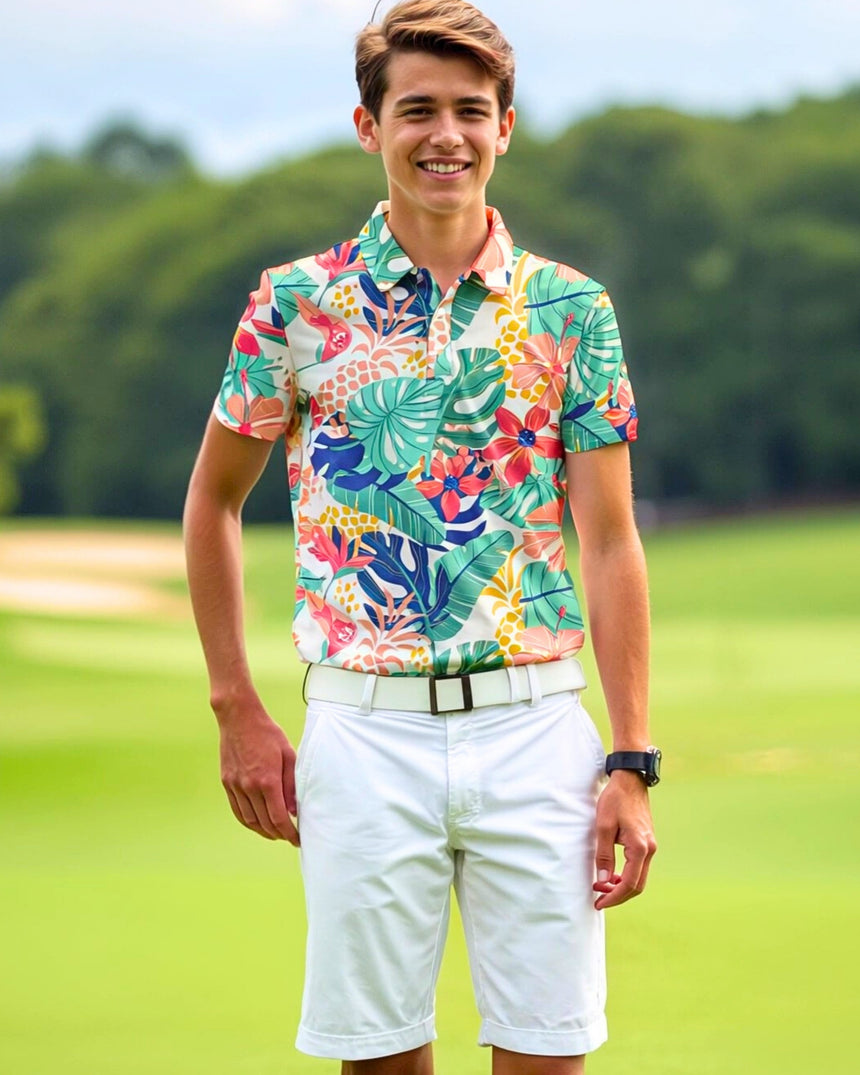 A young man smiles wearing a floral golf polo, white shorts, and a white belt on a golf course.