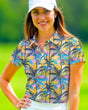 A woman smiles wearing a golf polo with a yellow background and a pattern of palm trees in shades of blue, pink, and black.