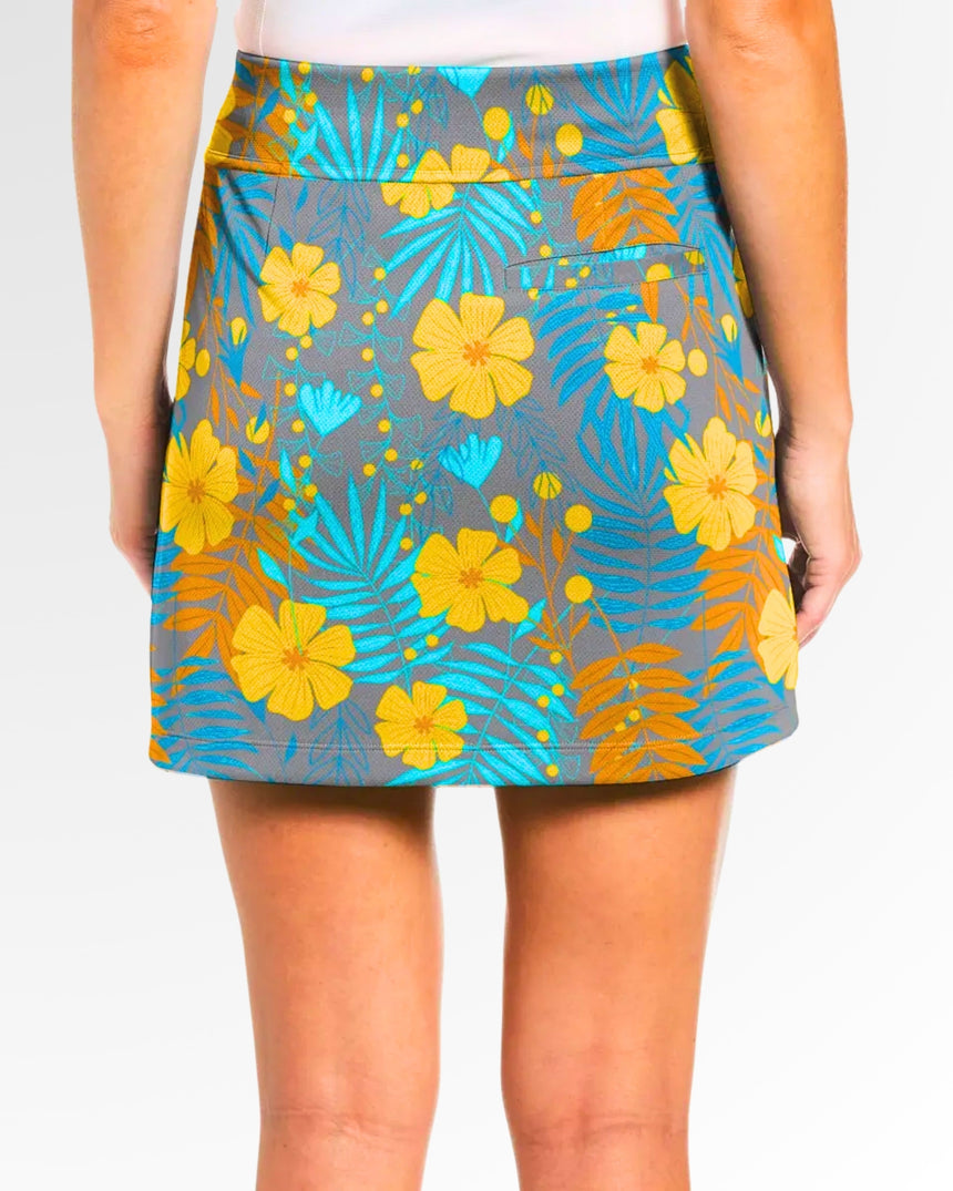 Close-up back view of a woman wearing a golf skort with a gray background and a floral pattern with yellow flowers and blue and orange leaves.