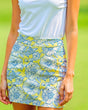 Close-up of a woman wearing a white golf polo and a yellow golf skirt with a white and blue floral pattern.