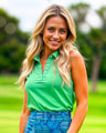 A woman smiles wearing a green sleeveless golf polo and a blue patterned golf skirt.
