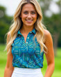 A smiling woman with long blonde hair and green eyes wears a blue patterned golf polo and white skirt.