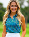 A smiling woman with long blonde hair and green eyes wears a blue patterned golf polo and white skirt.
