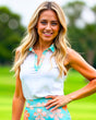 A blonde woman smiles at the camera, wearing a white golf polo with a floral collar and matching skirt.
