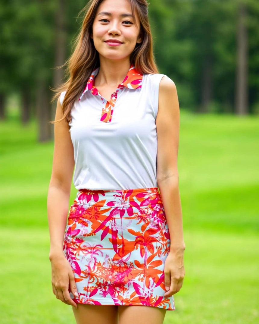 A woman stands on a golf course wearing a sleeveless white golf polo with a floral collar and a matching floral golf skirt.