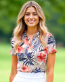 Woman wearing a floral patterned polo shirt with a blurred green background