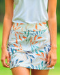 Woman wearing a white top and colorful floral golf skirt on a green background