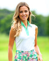 Woman wearing a white sleeveless top with green trim and floral skirt on a blurred green background