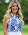 Woman wearing a blue floral sleeveless golf polo top with a blurred green background