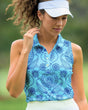 Woman wearing a blue floral patterned sleeveless golf top on a blurred green background