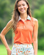 Woman wearing an orange sleeveless polo shirt with a floral skirt outdoors