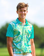Young boy wearing a green and white patterned golf shirt on a blurred outdoor background
