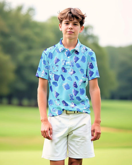 Young teenage boy wearing a blue patterned golf shirt and white shorts standing on a grassy field.