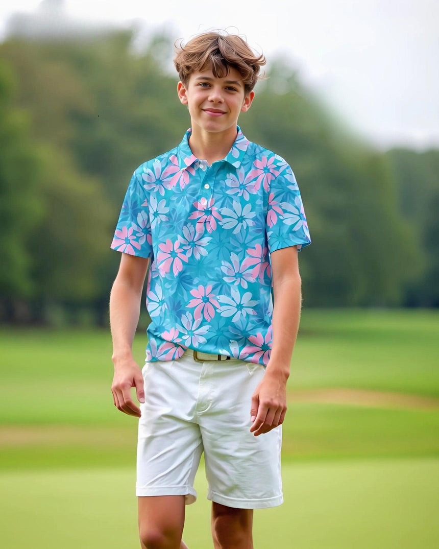 Young boy wearing a blue floral golf polo and white shorts standing on a grassy field.